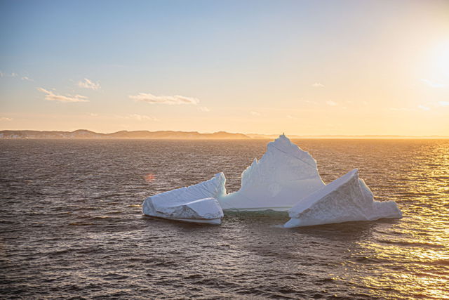 A frozen cathedral drifting in golden light  where the Arctic whispers to the Atlantic and the sunset bows in awe
